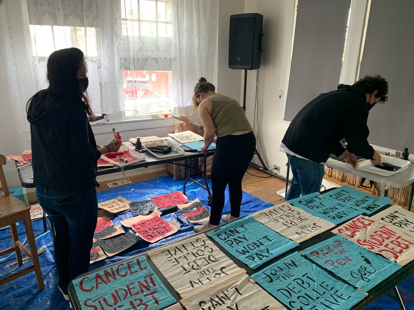 Three volunteers create screen printed cloth signs for a protest.